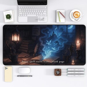 May include: A rectangular desk mat with a fantasy illustration of a book, dragons, and a castle. The mat has the text "Every spell starts with a blank page". The colour scheme includes blues, browns, and oranges.