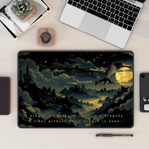 以下が含まれることがあります： 暗い雲の風景と満月の上を飛ぶ金の龍が描かれた黒いラップトップ。ラップトップには「龍がいない騎士は悲劇。騎士がいない龍は死んでいる。」という引用が印刷されている。