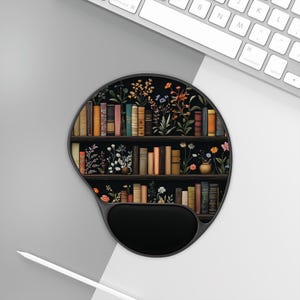 May include: A black and brown round mouse pad with a design of a bookshelf filled with books and flowers. The mouse pad has a black wrist rest.