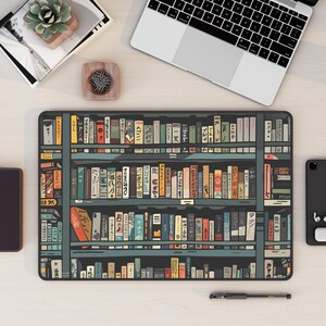 May include: A black and white illustration of a bookshelf filled with colourful books. The books have Japanese text on their spines. The bookshelf is on a light wood surface.