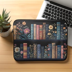Puede incluir: Una funda para portátil negra con un diseño de una estantería llena de libros coloridos y flores. Los libros están dispuestos en dos filas en la estantería, con flores que crecen entre ellos.