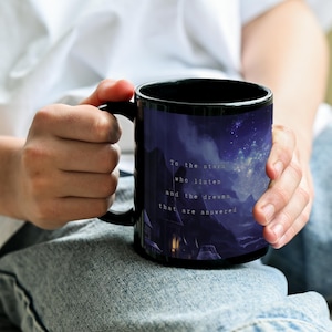 K&ouml;nnte beinhalten: Schwarze Keramik-Tasse mit einer malerischen Illustration eines Sternenhimmels &uuml;ber einer Bergkette. Die Tasse tr&auml;gt den Text "To the stars who listen and the dreams that are answered."