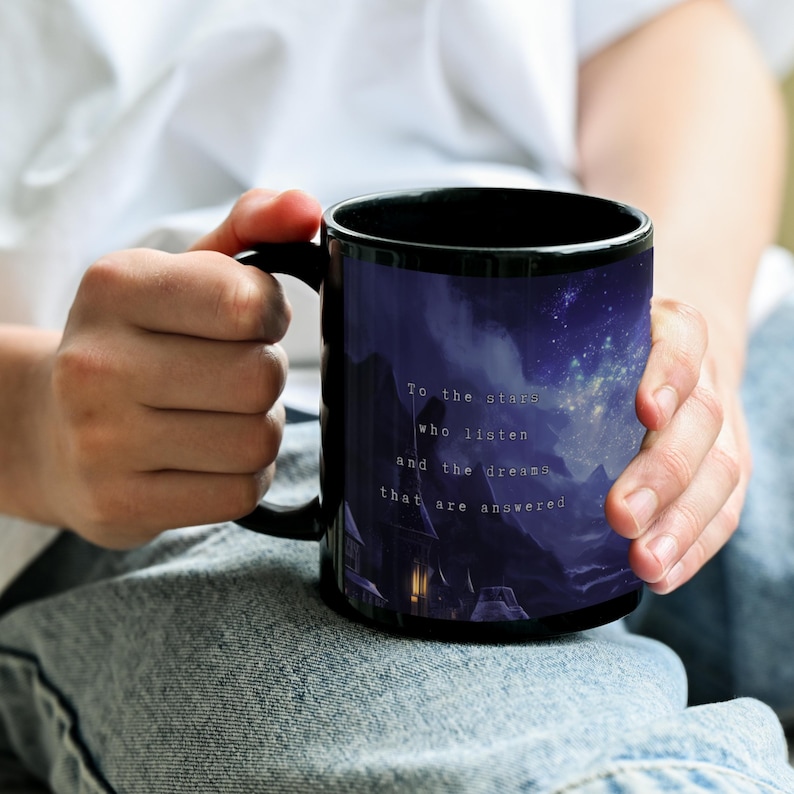 K&ouml;nnte beinhalten: Schwarze Keramik-Tasse mit einer malerischen Illustration eines Sternenhimmels &uuml;ber einer Bergkette. Die Tasse tr&auml;gt den Text "To the stars who listen and the dreams that are answered."