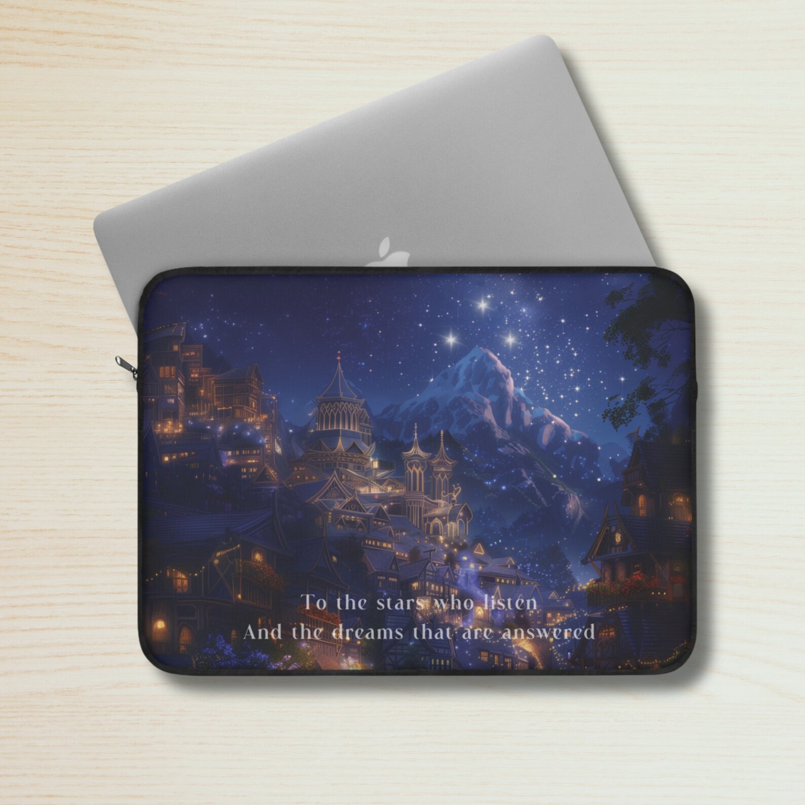 A laptop sleeve sitting on top of a gray laptop on a light wooden background. The sleeve depicts an elaborate golden and blue city lit with many street and house lights, and a blue night sky with stars and a mountain in the background.