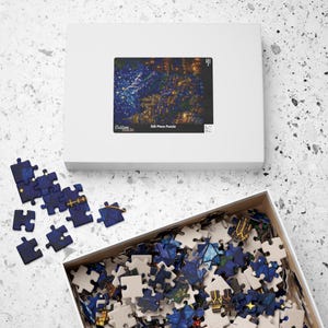 May include: A white rectangular puzzle box featuring a dark blue night sky illustration with golden buildings and stars. The box lid displays the text Custom made and 520 Piece Puzzle. Several loose blue puzzle pieces lie nearby.