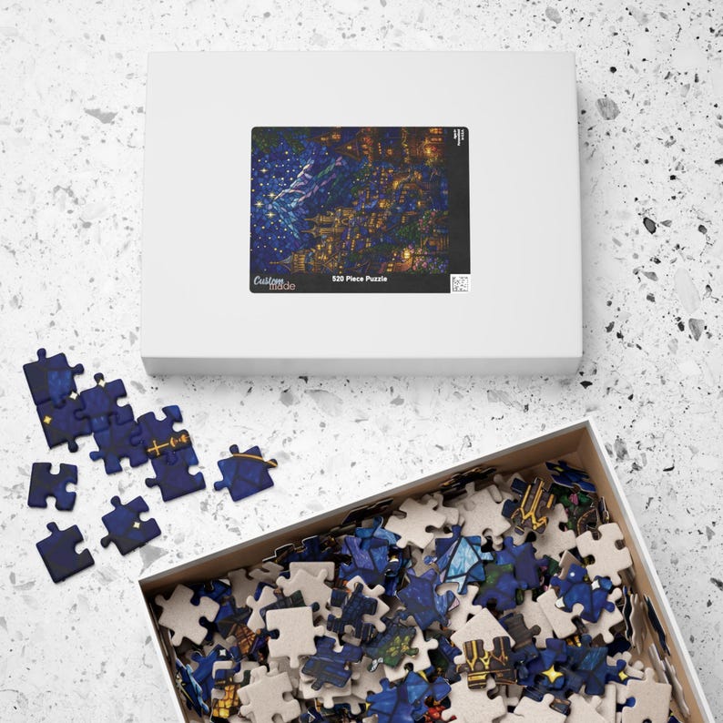 May include: A white rectangular puzzle box featuring a dark blue night sky illustration with golden buildings and stars. The box lid displays the text Custom made and 520 Piece Puzzle. Several loose blue puzzle pieces lie nearby.
