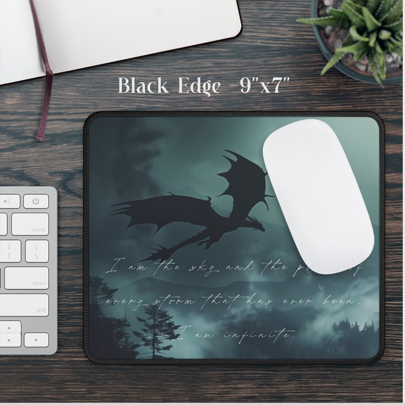 May include: A black mouse pad with a dark green and blue background featuring a silhouette of a dragon flying through the clouds. The text "I am the sky and the proof of every storm that has ever been. I am infinite." is printed on the mouse pad.
