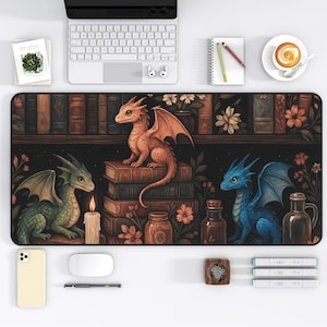 May include: A desk mat featuring a fantasy scene with three dragons of different colors: orange, green, and blue. The dragons are perched on books in front of a bookshelf with flowers and jars. A keyboard, phone, and coffee cup are also visible.