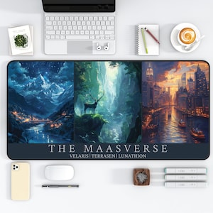 May include: A black and blue mousepad with three different scenes: a snowy mountain range, a forest with a deer, and a cityscape at sunset. The mousepad has the text "THE MAASVERSE VELARIS|TERRASEN|LUNATHION" printed on it.