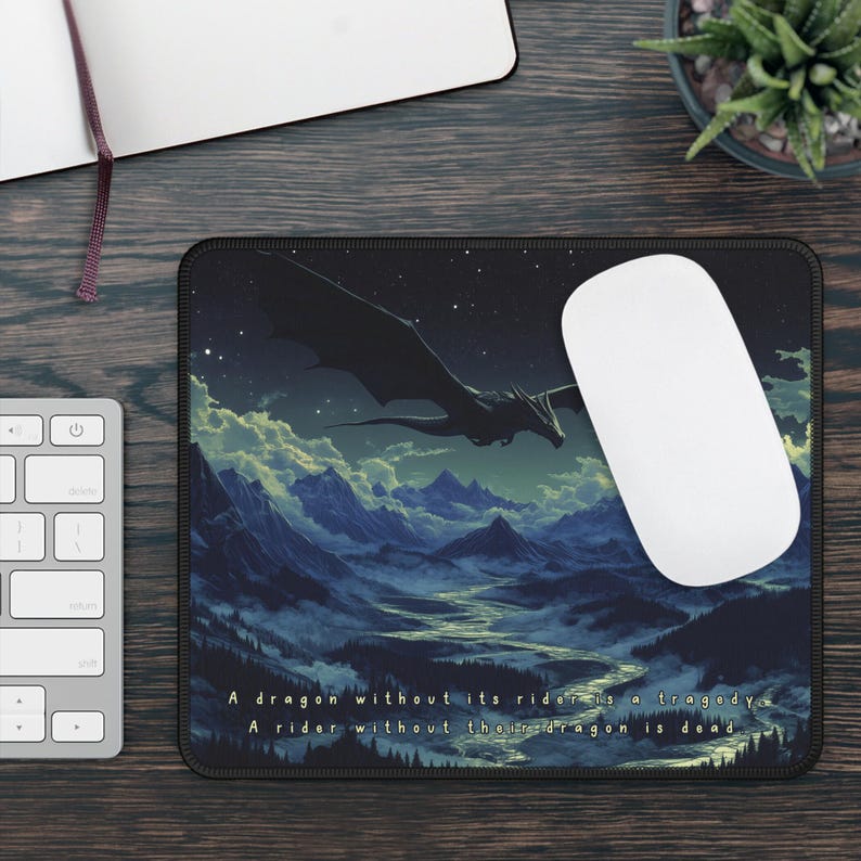 May include: A black mousepad with a dark blue and green landscape scene featuring a black dragon flying over mountains. The text "A dragon without its rider is a tragedy. A rider without their dragon is dead." is printed at the bottom of the mousepad.