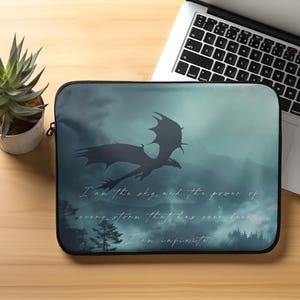 May include: A laptop sleeve with a dark blue background featuring a silhouette of a dragon flying through a misty forest. The text "I am the sky and the power of every storm that has ever been. I am infinite." is printed in white on the sleeve.