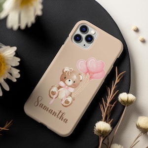May include: A beige phone case with a brown teddy bear holding pink heart-shaped balloons. The text "Samantha" is printed on the case.
