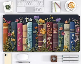May include: A decorative desk mat featuring a row of colorful, textured books adorned with various flowers. The books are in shades of orange, pink, blue, and green, with detailed floral embellishments. The mat is surrounded by a dark blue border, and a white desk, keyboard, and accessories are visible.