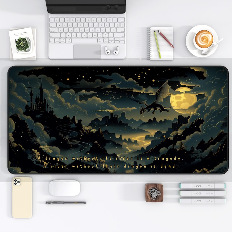 以下が含まれることがあります： 星が輝く夜空を飛ぶドラゴンが描かれた、黒と金のマウスパッド。マウスパッドには、「ドラゴンがライダーなしでは悲劇。ライダーがドラゴンなしでは死んでいる。」というテキストが書かれている。