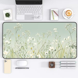 May include: A rectangular desk mat with a floral design featuring white flowers and green foliage against a soft green background. The mat is surrounded by office supplies, including a keyboard, phone, and coffee cup.