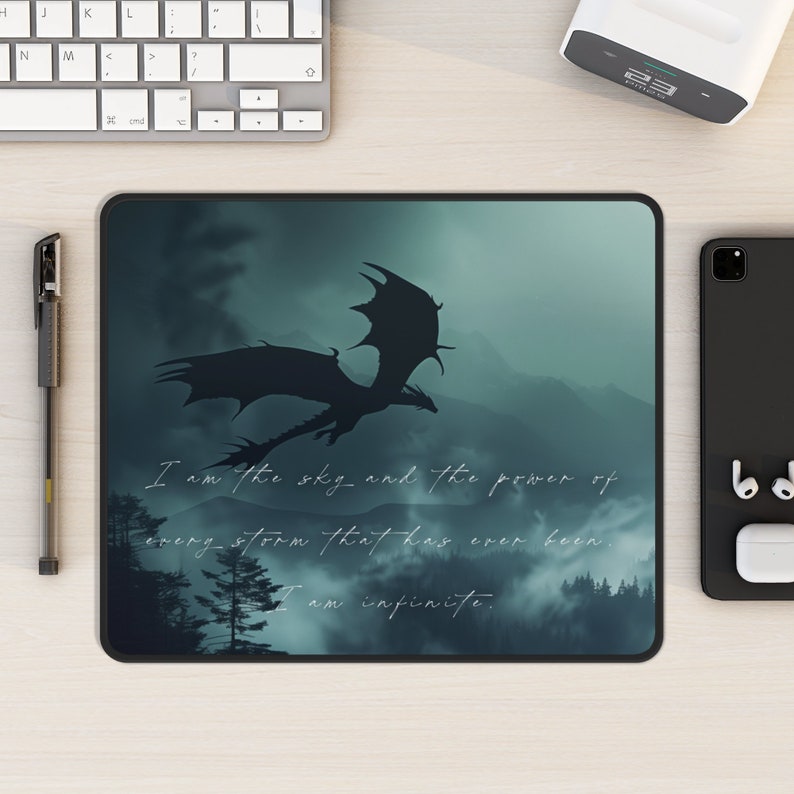 May include: A dark blue mousepad with a silhouette of a dragon flying over a misty forest. The text "I am the sky and the power of every storm that has ever been. I am infinite." is printed on the mousepad.