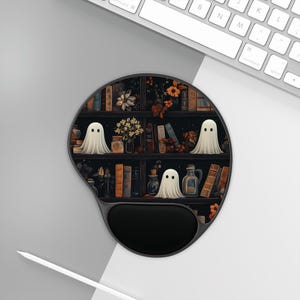 May include: A black and white mouse pad with a design of a bookshelf filled with books and three white ghosts. The bookshelf is decorated with flowers and other decorative items.