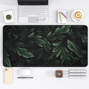 May include: A black and green mousepad with a leafy pattern. The mousepad is on a white desk with a laptop, a phone, a cup of coffee, and other office supplies.