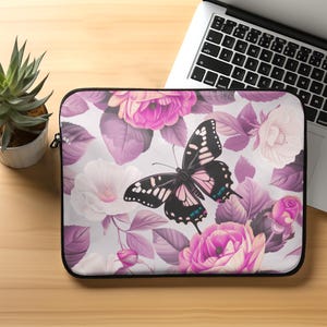 May include: A laptop sleeve with a floral pattern featuring pink roses and a black butterfly with pink accents. The background is white with purple leaves.