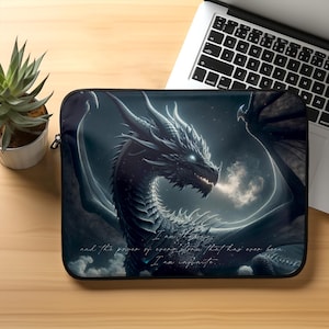 Puede incluir: Una funda para portátil negra con un dragón azul oscuro que escupe fuego. El dragón está sobre un fondo azul oscuro con estrellas blancas. El texto "I am the change... and the power of evolution that has ever been. I am infinite." está impreso en la funda.