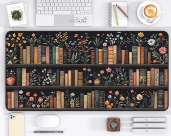 May include: A black desk mat featuring a bookshelf design with colorful flowers and vintage books. The mat has a rectangular shape and is surrounded by office supplies, including a keyboard, mouse, and phone.
