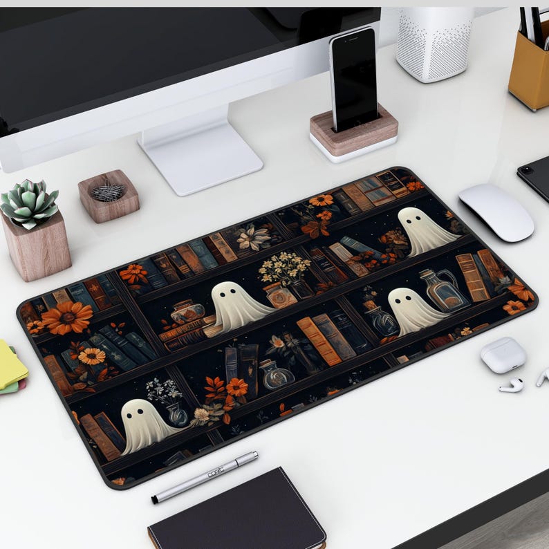 Puede incluir: Una alfombrilla de rat&oacute;n negra y blanca con un dise&ntilde;o de una estanter&iacute;a llena de libros, flores y fantasmas. Los fantasmas son blancos y transl&uacute;cidos.