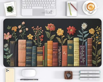 May include: A black desk mat featuring a row of colorful, textured books with embroidered flowers. The mat has a variety of books in shades of brown, orange, green, and blue. The flowers are in shades of pink, yellow, and red.