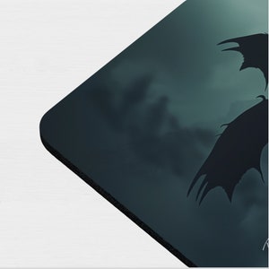 May include: A dark blue and black mousepad with a silhouette of a dragon flying through a stormy sky.