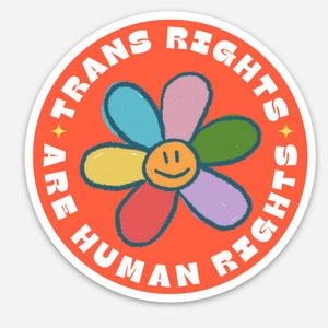 May include: A round sticker with an orange background and a white border. The sticker features a colorful flower with a smiley face in the center. The text around the flower reads "Trans Rights Are Human Rights".