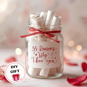 May include: A clear glass jar filled with rolled-up white paper scrolls, tied with a red ribbon. A white label on the jar reads "55 Reasons Why I love you" in red script. The jar is a DIY gift.