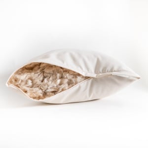 May include: A cream-colored pillow with a partially open seam, revealing a fluffy, light brown filling. The pillow is made of a soft, natural fabric, and the filling appears to be a loose, fibrous material. The design suggests a focus on comfort and natural materials.