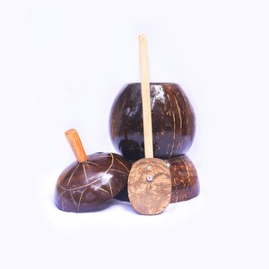 以下が含まれることがあります： 手作りのココナッツ殻のボウルと調理器具のコレクション。ボウルは濃い茶色で、自然な質感の仕上がりです。木のスプーンと木の取っ手が付いた蓋も含まれています。白い背景に配置されています。