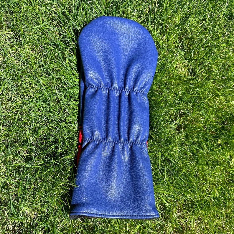 Puede incluir: Una funda para la cabeza de un palo de golf de cuero azul con costuras rojas.