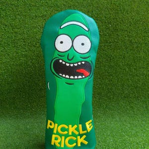 May include: A green golf club head cover with a cartoon pickle character design. The cover has large white eyes, a wide open mouth, and the text "Pickle Rick" in yellow. The cover is made of a soft material.