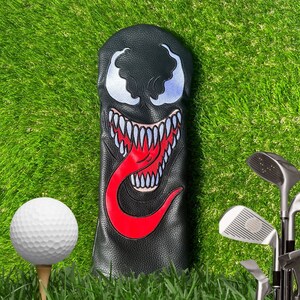 K&ouml;nnte beinhalten: Schwarzer Golfschl&auml;gerkopfbezug mit einem roten und wei&szlig;en Venom-Charakterdesign. Der Charakter hat einen gro&szlig;en Mund mit scharfen Z&auml;hnen und einer roten Zunge.
