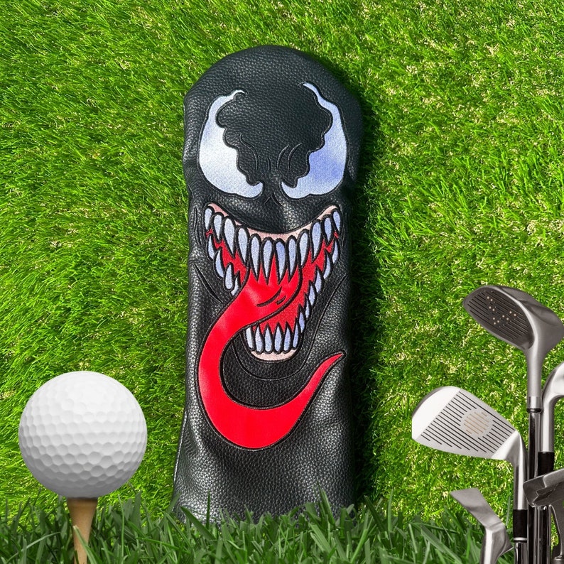 K&ouml;nnte beinhalten: Schwarzer Golfschl&auml;gerkopfbezug mit einem roten und wei&szlig;en Venom-Charakterdesign. Der Charakter hat einen gro&szlig;en Mund mit scharfen Z&auml;hnen und einer roten Zunge.