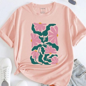 May include: A pink t-shirt with a floral print featuring pink flowers and green leaves. The shirt has a crew neck and short sleeves.