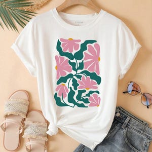 May include: White t-shirt with a pink and green floral print. The shirt has a crew neck and short sleeves. The print features stylized flowers and leaves.
