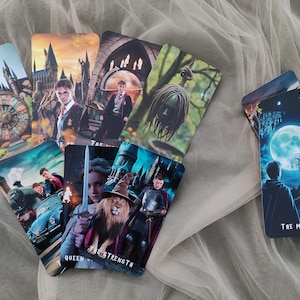 Könnte beinhalten: Eine Sammlung von Tarotkarten mit Fantasy-Illustrationen. Die Karten zeigen Charaktere, Burgen und Szenen mit Titeln wie "Der Mond" und "Königin der Stärke". Die Karten sind auf einem weichen, weißen Stoff angeordnet.