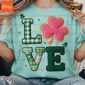 May include: A light blue t-shirt with the word "LOVE" in a patchwork design. The "L" is green and white checkered, the "O" is a pink shamrock, the "V" is green and patchwork, and the "E" is dark green. Small green hats and stars are scattered around the letters.