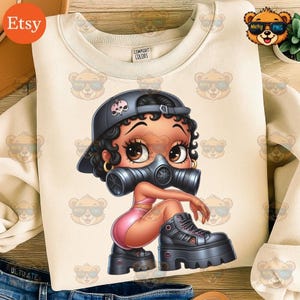 May include: Cream-colored sweatshirt featuring a cartoon illustration of a woman wearing a gas mask, black cap with a skull, and platform boots. The design is in a pop art style. The sweatshirt has the Comfort Colors brand label.