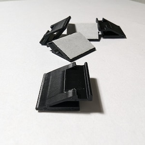 May include: Five black plastic corner brackets with adhesive backing. The brackets are designed to be used for mounting shelves or other objects to a wall.