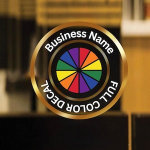 May include: A circular full-color decal with a gold border. The center features a color wheel design with segments in red, orange, yellow, green, blue, and purple. The text "Business Name" and "FULL COLOR DECAL" are in white.