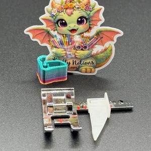 May include: A sticker of a cartoon dragon with a flower crown, holding pencils and scissors, with the text "My Notions com". A sewing machine foot and a 3D-printed object are also in the image.