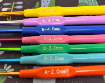 May include: A set of seven colourful crochet hooks with size labels: G-5.0mm, F-4.5mm, E-4.0mm, D-3.5mm, C-3.0mm, B-2.5mm, and A-2.0mm.