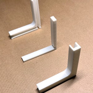 May include: Three white plastic corner brackets, each with a 90-degree angle. The brackets are designed to connect two pieces of wood or other materials at a right angle.