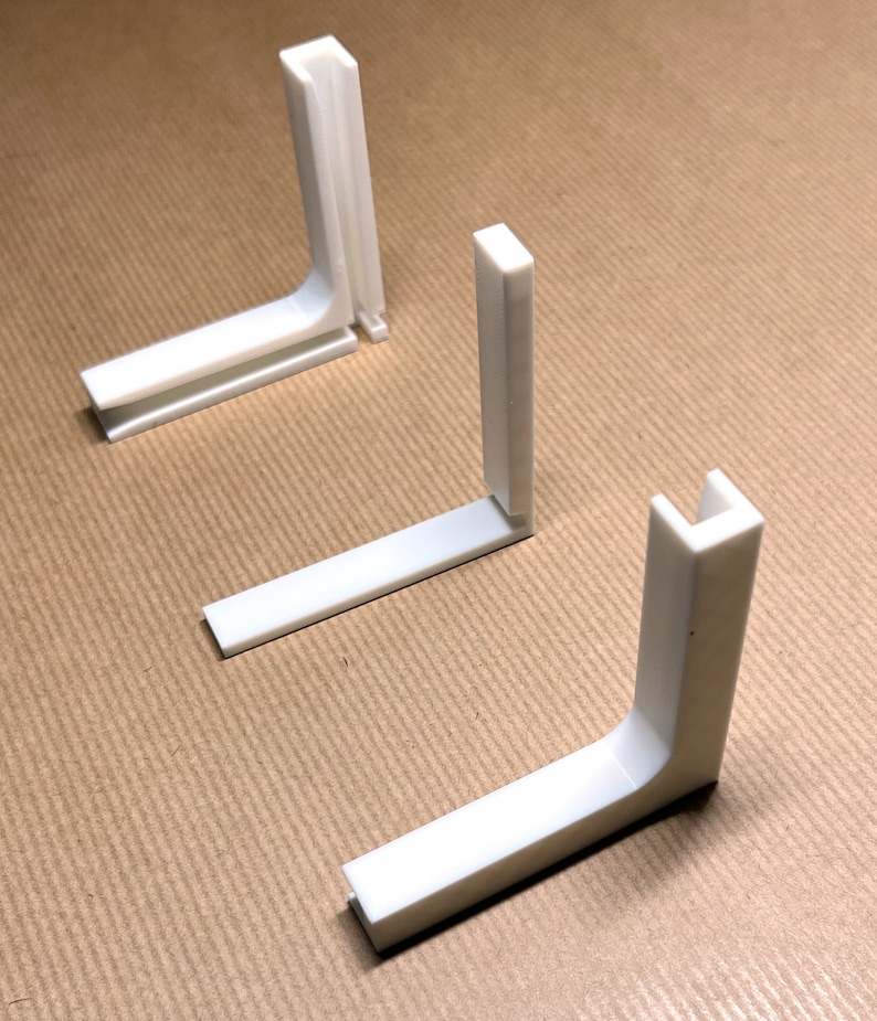 May include: Three white plastic corner brackets, each with a 90-degree angle. The brackets are designed to connect two pieces of wood or other materials at a right angle.