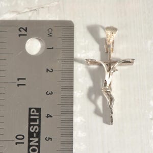 May include: A silver crucifix pendant. The pendant is approximately 5 cm in length and depicts Jesus on the cross in detail. The cross is positioned next to a ruler with cm measurements.
