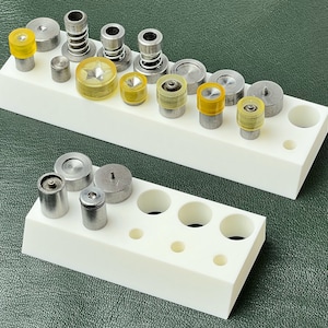 May include: A white plastic organizer with two rows of compartments, each holding various sized metal and yellow plastic snap fasteners.