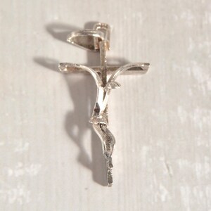 May include: A silver crucifix pendant with a detailed depiction of Jesus. The pendant has a textured surface and is suspended from a small loop. The cross arms are slightly curved.
